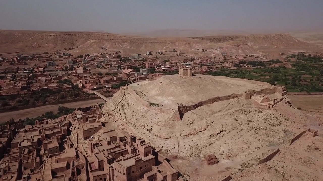 Ripresa cinematografica con drone delle iconiche rovine del granaio in cima alla collina che dominano l'antico villaggio di mattoni di fango di Ait Benhaddou, un sito Patrimonio dell'Umanità UNESCO in Marocco.