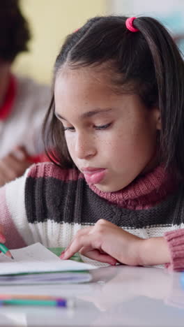 young girl writing in notebook, sitting at a desk in a classroom