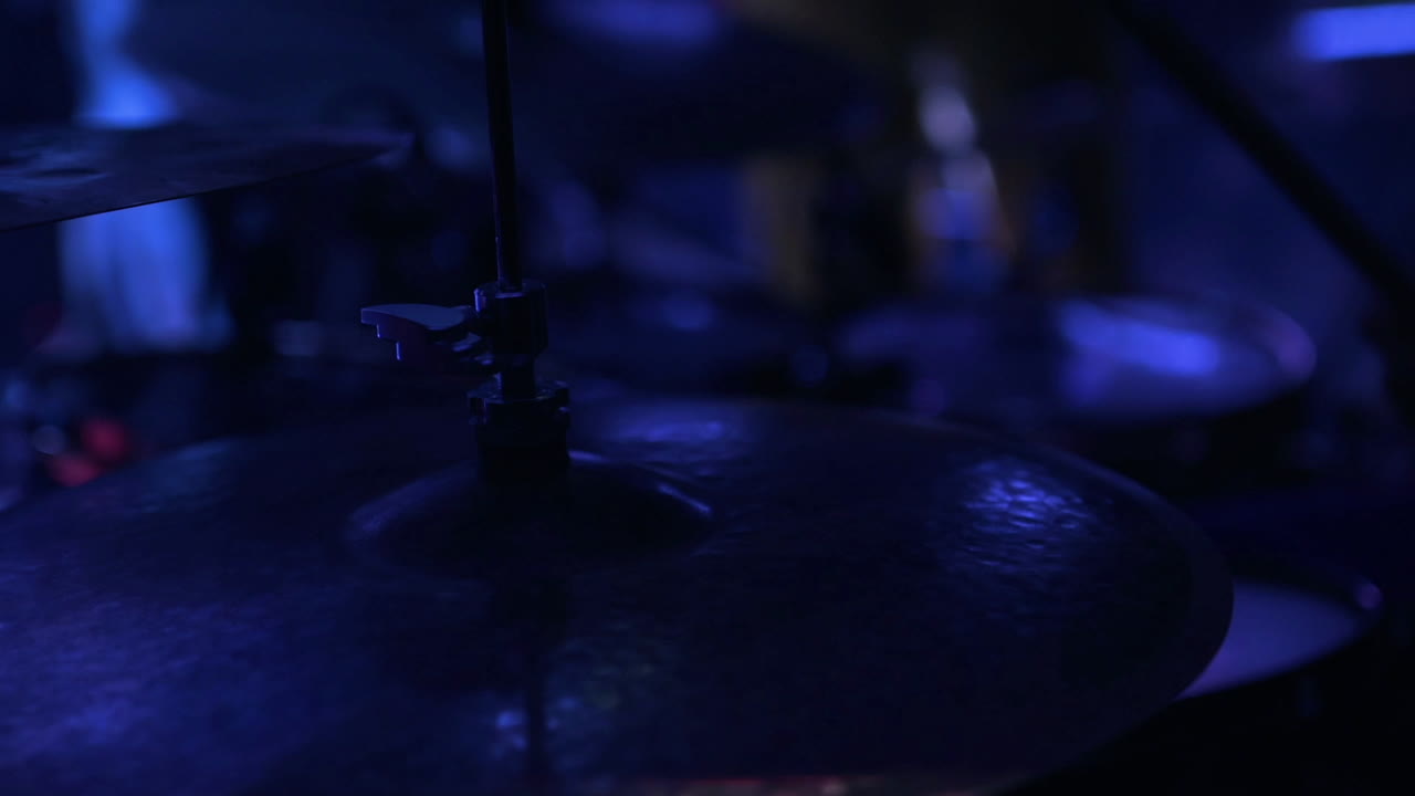 Primo piano di un batterista che suona i piatti con illuminazione scenica colorata.