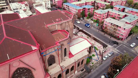 Dolly-in-aerial-view-of-the-back-of-the-Basilica-Salvador-in-dilapidated-and-weathered-condition,-broken-stained-glass-windows-and-an-old-housing-complex-in-Santiago-Chile