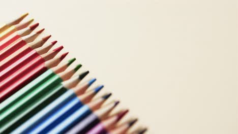 vista aérea de lápices de colores dispuestos con espacio de copia sobre fondo beige, en cámara lenta