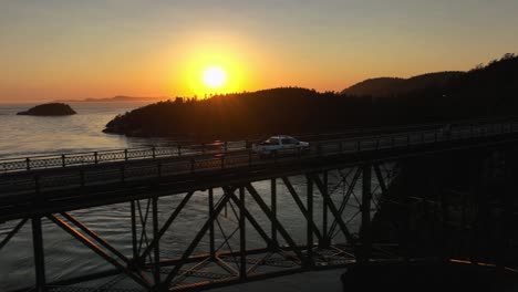 Aerial-shot-of-a-Park-Ranger's-truck-driving-over-Deception-Pass-Bridge-at-sunset