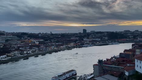 drone footage captures douro river in porto during sunset, with boats floating near riverside and city skyline under dramatic sky. soft light highlights rooftops and calm water reflecting sky tones