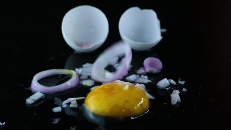 cáscara de huevo blanca agrietada con clara de huevo y yema cubierta por anillos de cebolla rebanados que caen