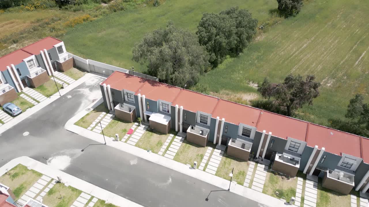 Backward Drone Aerial Motion From Small Rural Homes Toward Large Private Housing Complex Expanding Into Green Farmland in Mexico – Sunny 4K