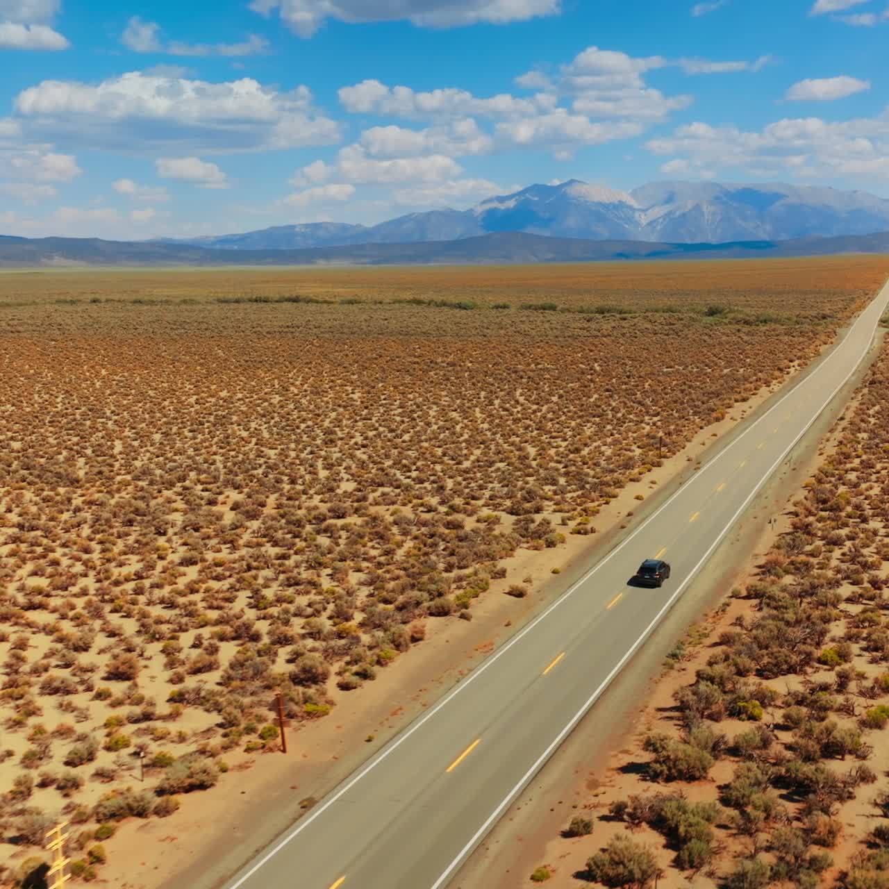 Following the black cars riding by the empty road through the deserted land. Highway from California to Nevada footage on sunny day. Mountain at backdrop