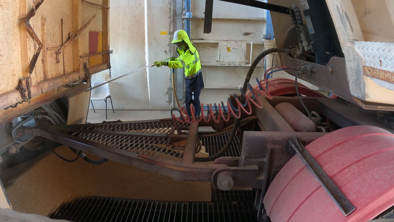 Footage of a harvest worker using an air gun to clean remaining grain from a truck bed at a grain reception and storage facility in Western Australia.