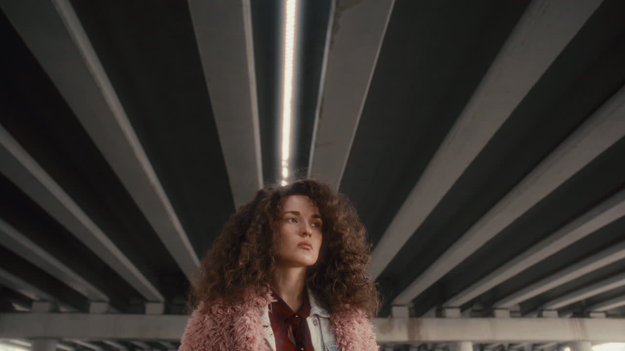 Beautiful Curly-Haired Girl Standing under Urban Bridge, Looking into Distance