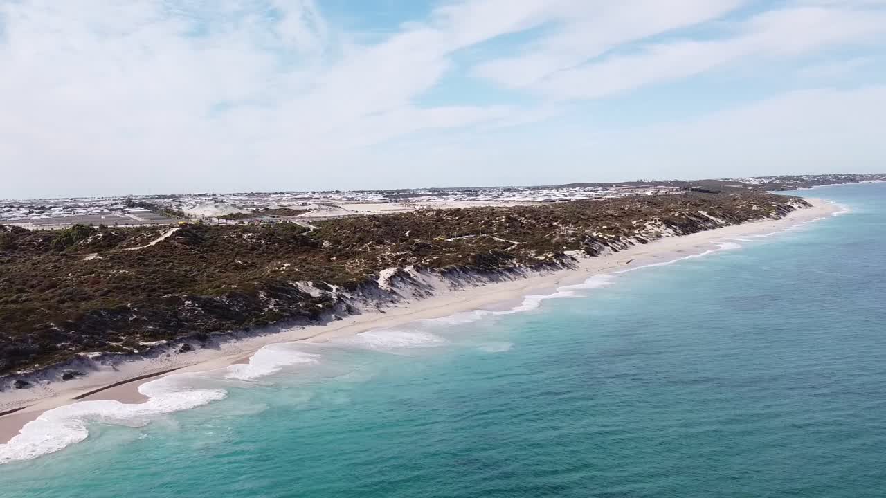 vista aérea de las olas que se estrellan en la playa de edén con dunas y casas en el fondo