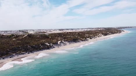 Aerial-view-of-waves-crashing-on-Eden-Beach-with-dunes-and-houses-in-background