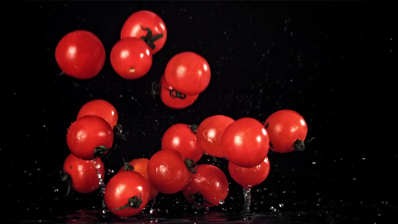 Tomates cherry rojos frescos cayendo y salpicando sobre una superficie negra mojada