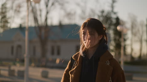 a girl wearing a brown coat and a hoodie is walking faintly, with an expression of weariness and contemplation. her hair is gently tousled by the wind, moment of quiet reflection in an urban setting