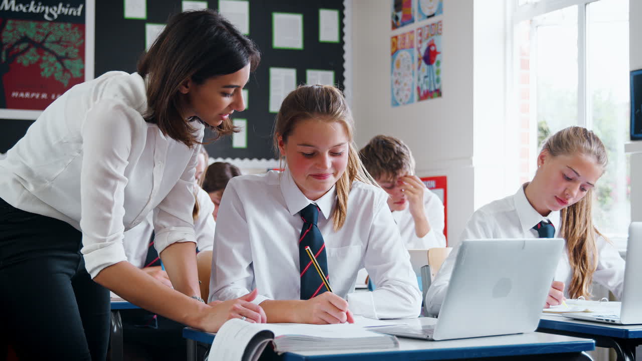 maestra ayudando a la alumna a usar la computadora en el aula