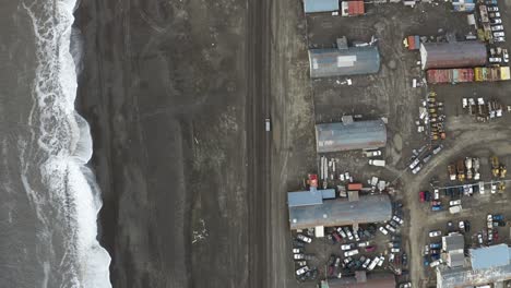 Toma-Aérea-De-Seguimiento-De-Arriba-Hacia-Abajo-De-Una-Furgoneta-Que-Conduce-A-Lo-Largo-De-Una-Carretera-Inundada-Junto-Al-Océano-ártico-Y-Estructuras-Deterioradas-Cerca-De-Barrow-Alaska