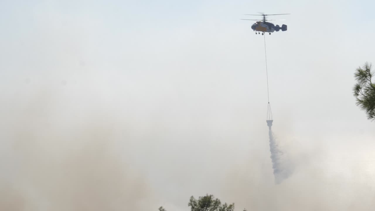 imágenes de un helicóptero de extinción de incendios mientras sobrevuela un incendio forestal y arroja su cubo de agua sobre el fuego para apagar las llamas.