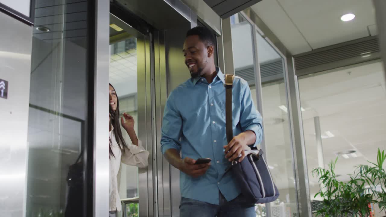 Video of happy diverse woman and man walking outside elevator and talking