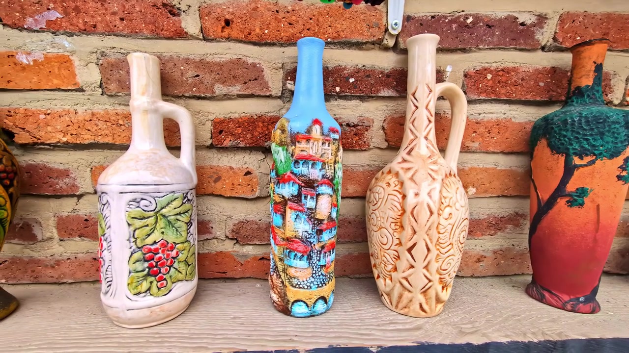 Bottiglie decorative artigianali esposte su uno scaffale di legno contro un muro di mattoni.
