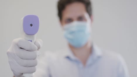 retrato de un hombre con una máscara en la cara sosteniendo una pistola de temperatura