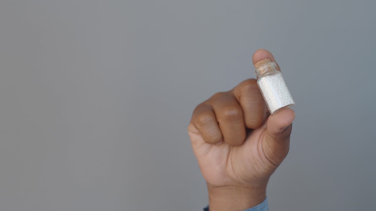 una mano sosteniendo una pequeña botella con pastillas blancas