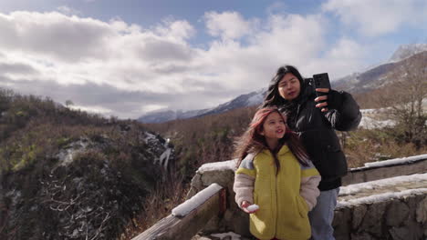 mother and daughter capture joyful selfie during winter trip in mountains