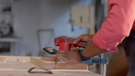 sanding senior african american man wearing apron using sander on plank clamped to workbench