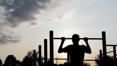 young male silhouette exercising pullups with resistance band at sunrise