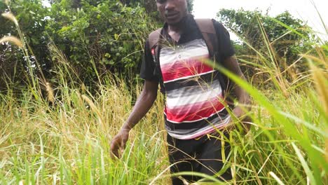 a very slow motion tracking shot from in front of a young african man pushing through tall grass in rural africa