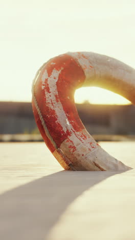 a red and white lifebuoy on a sandy beach with the sun setting in the background.