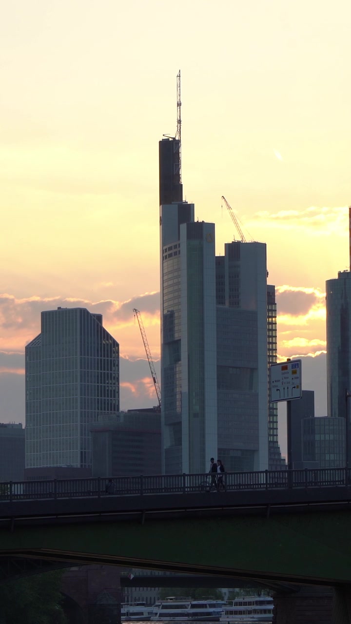 Rascacielos y grúas en silueta al atardecer con gente caminando por un puente de la ciudad