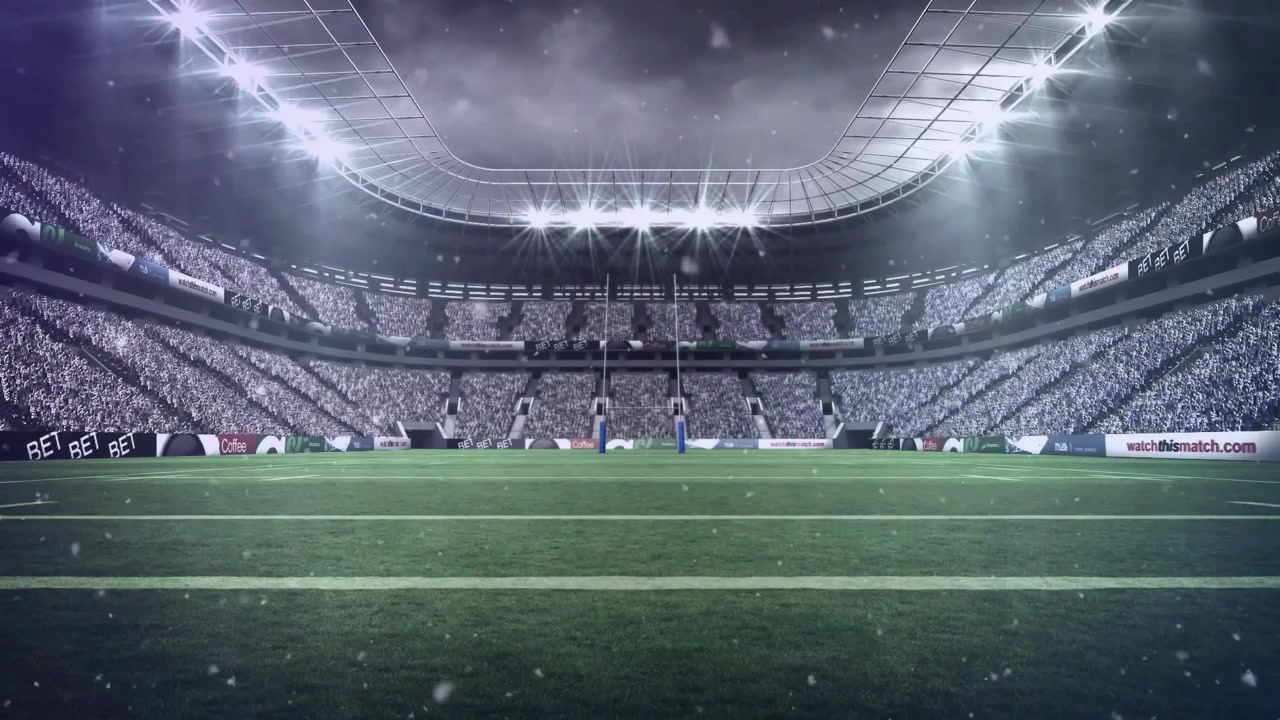 Inquadratura iniziale che rivela l'interno di uno stadio sportivo sotto i riflettori, con neve che si sposta creando atmosfera.