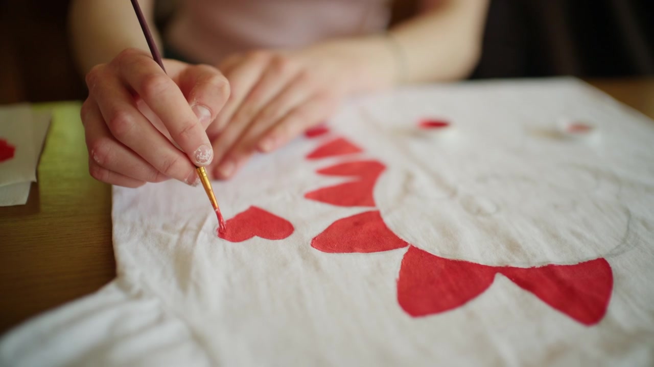 Primo piano di un artista che dipinge forme decorative rosse su una maglietta bianca usando pittura per tessuti