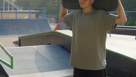 young boy in skatepark looking at camera smiling and holding a scooter behind his head