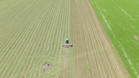 aerial and ground-level footage of a modern agricultural tractor driving across a green wheat field in rural bulgaria during spring