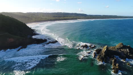 aerial shots over a stunning rock formation with waves crashing up against them on the coastline