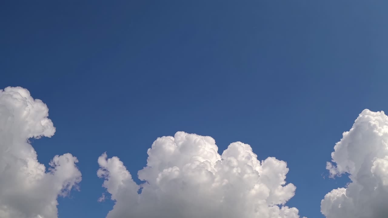 Video of fluffy white clouds against a clear blue sky, captured from a low angle, conveying a serene