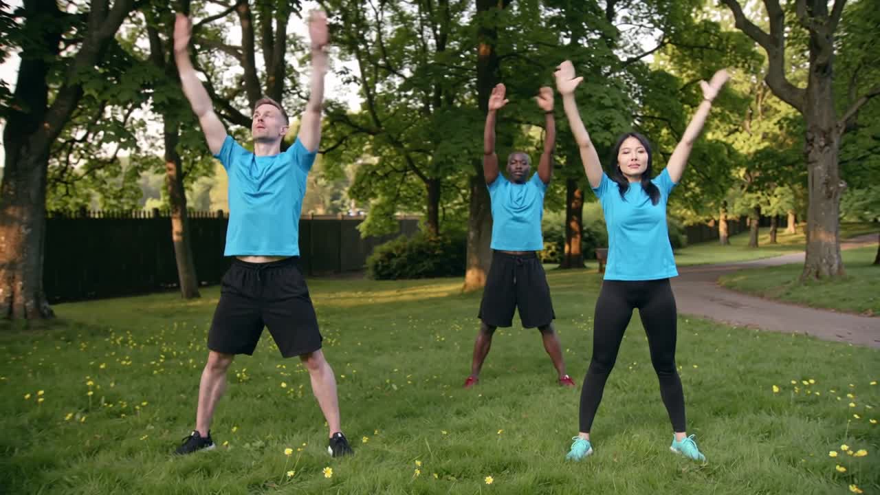Starting on cue, trio doing arm raises and side bends for warmup in park, blue shirts