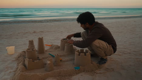 man building a sandcastle at the beach during sunset