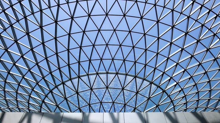 Camera tilts upward beneath a geometric glass dome, revealing a large indoor waterfall with natural daylight illuminating the architectural structure