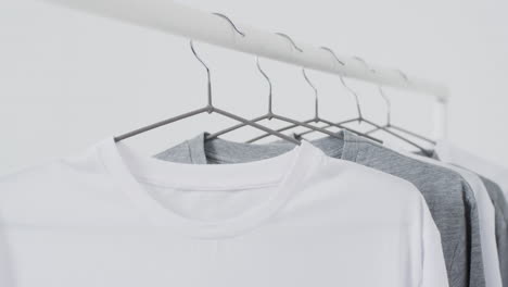 video of white and grey t shirts on hangers and copy space on white background