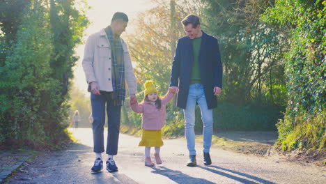 close up of family with two dads taking daughter for walk in fall or winter countryside