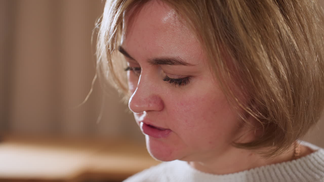 Close up of thoughtful woman reading from book in warm therapy lounge, immersed in focused expression as natural light highlights her face and quiet atmosphere encourages introspective engagement
