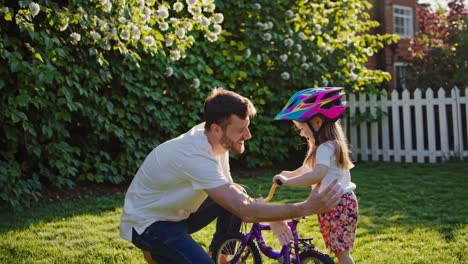 father teaching daughter to ride a bike in garden