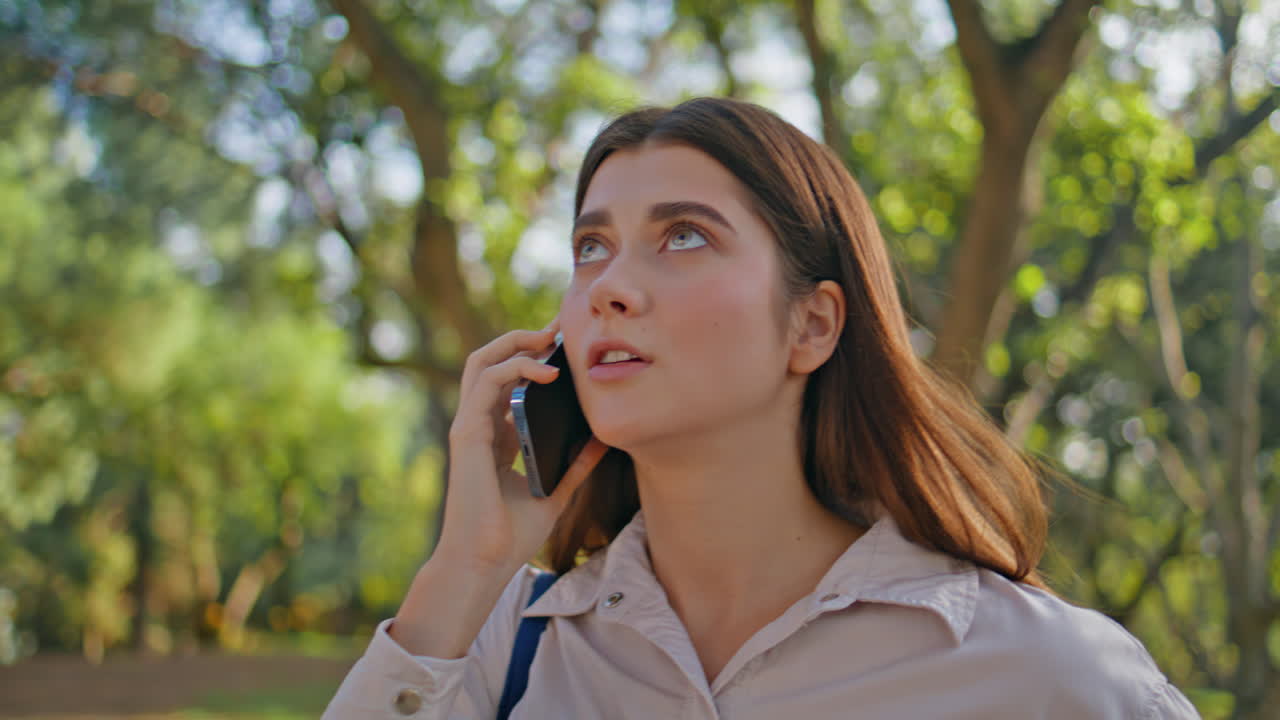 una mujer molesta hablando por teléfono móvil mirando frustrada caminando por el parque verde de cerca.