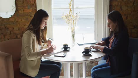 two caucasian businesswomen sitting at table with coffee, talking, having business meeting