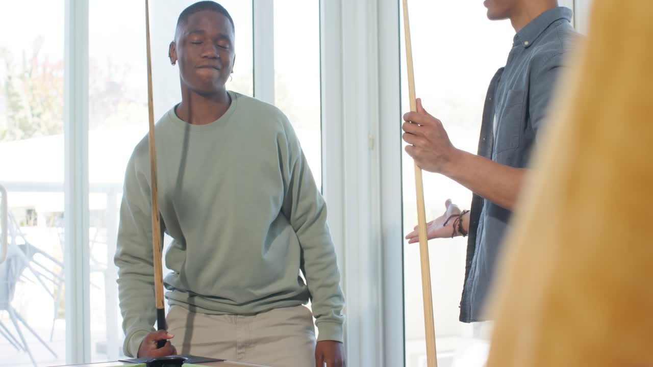 Diverse male friends aiming shot, striking ball and high-fiving on pool table with balls scattering