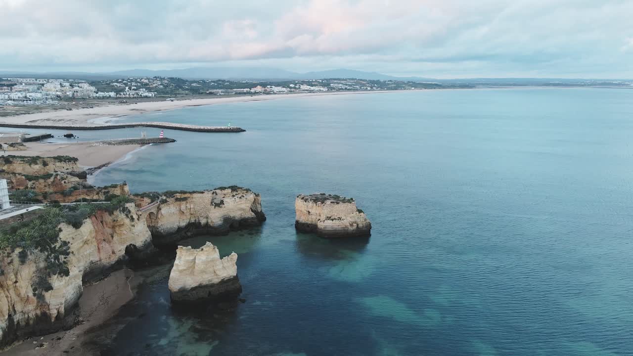 Aerial drone descends and pans upward, unveiling a sandy beach, cliffs, and the distant horizon of the Atlantic near Lagos