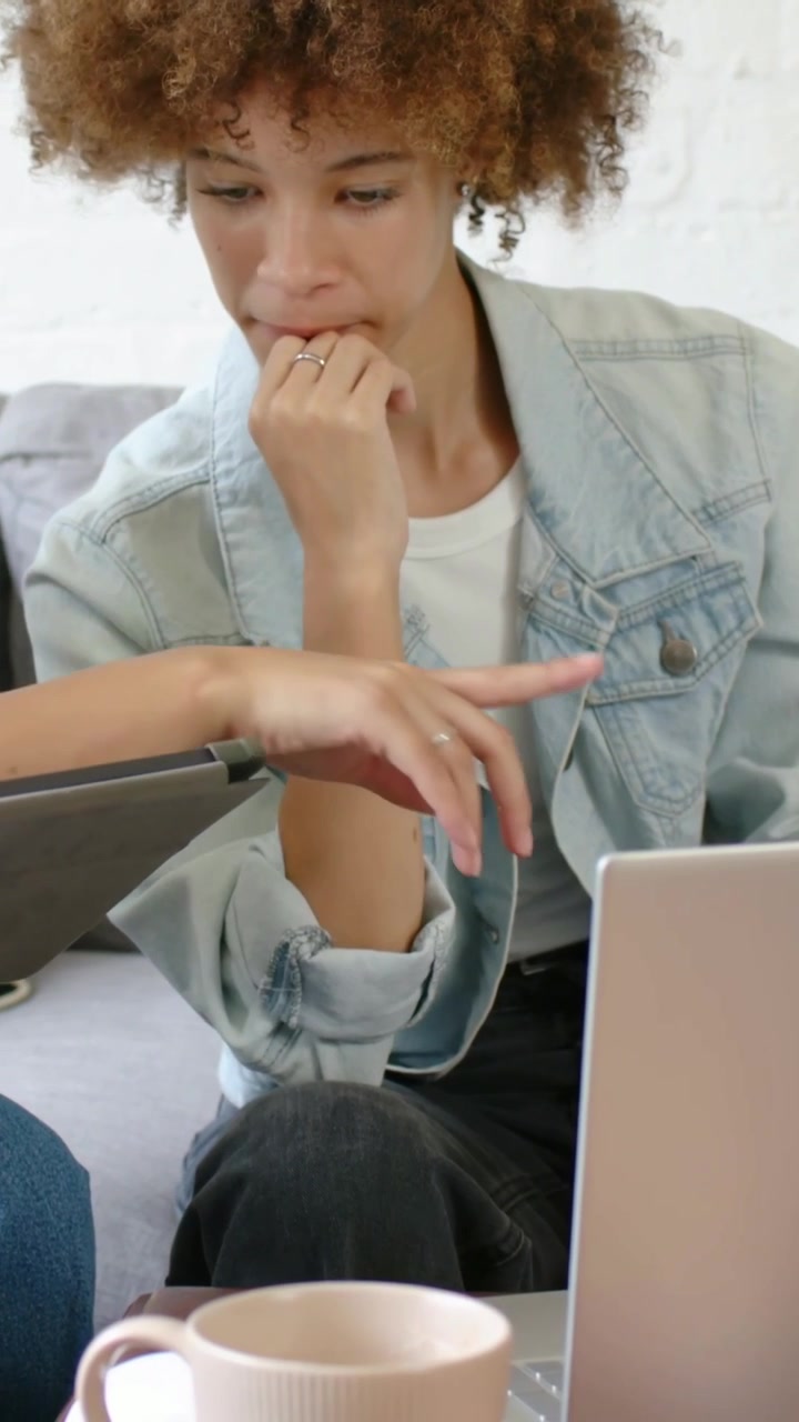 Video verticale: Mano sinistra che mostra un tablet, donna in giacca che si gira sul divano, controllando un laptop.