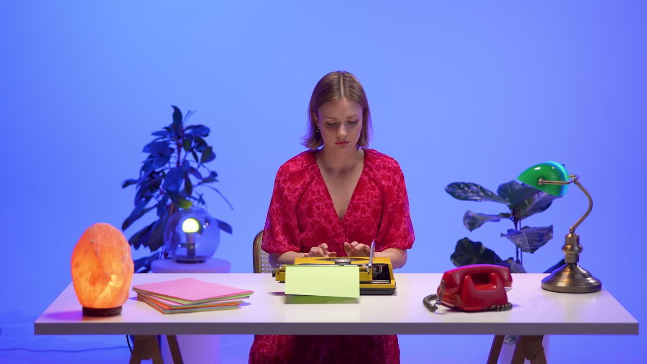 A woman in a floral red dress puts down a red rotary phone on her retro desk. Surrounded by a typewriter, pastel paper, and warm lamps, the scene captures a nostalgic and expressive office moment
