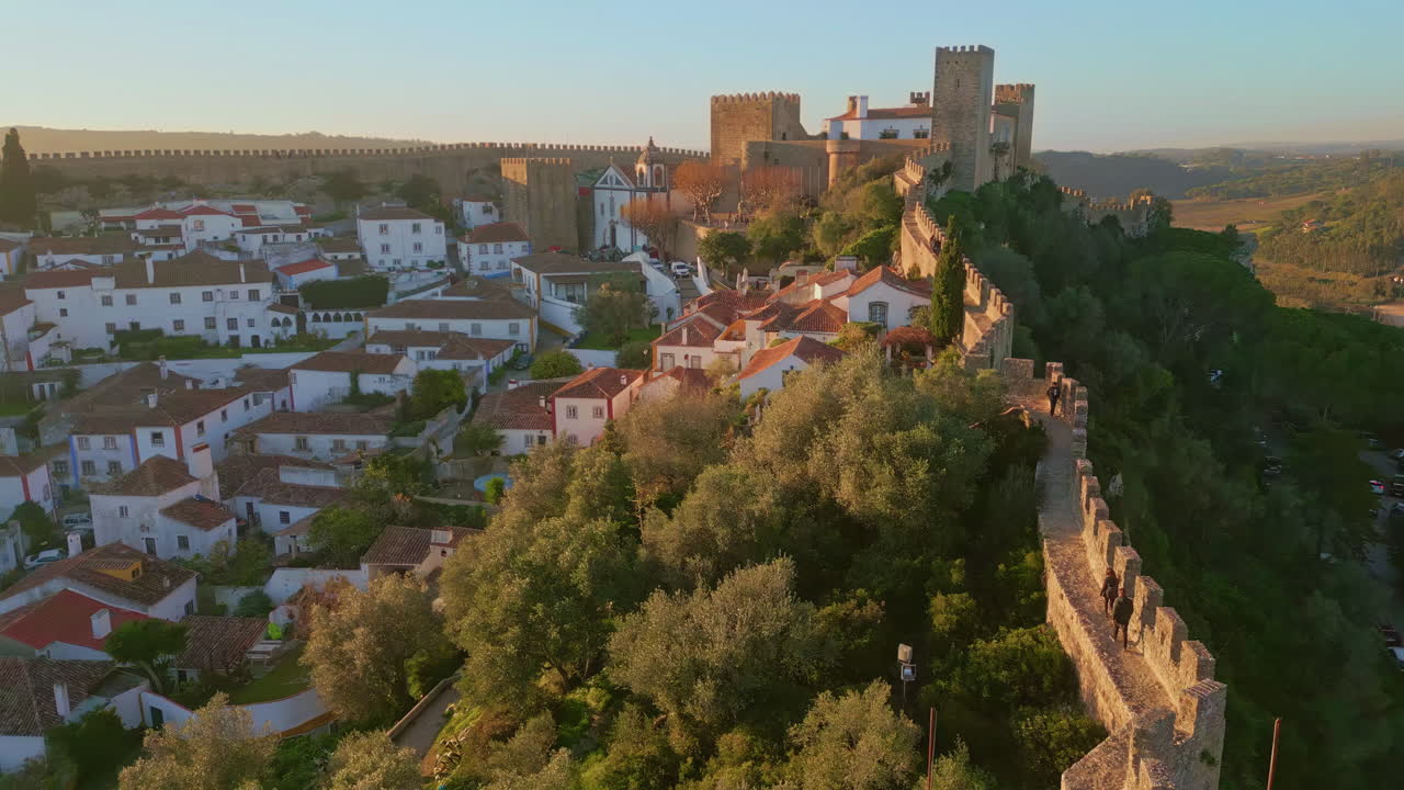 Stone castle towers towering over cozy old town at evening sunlight aerial view.