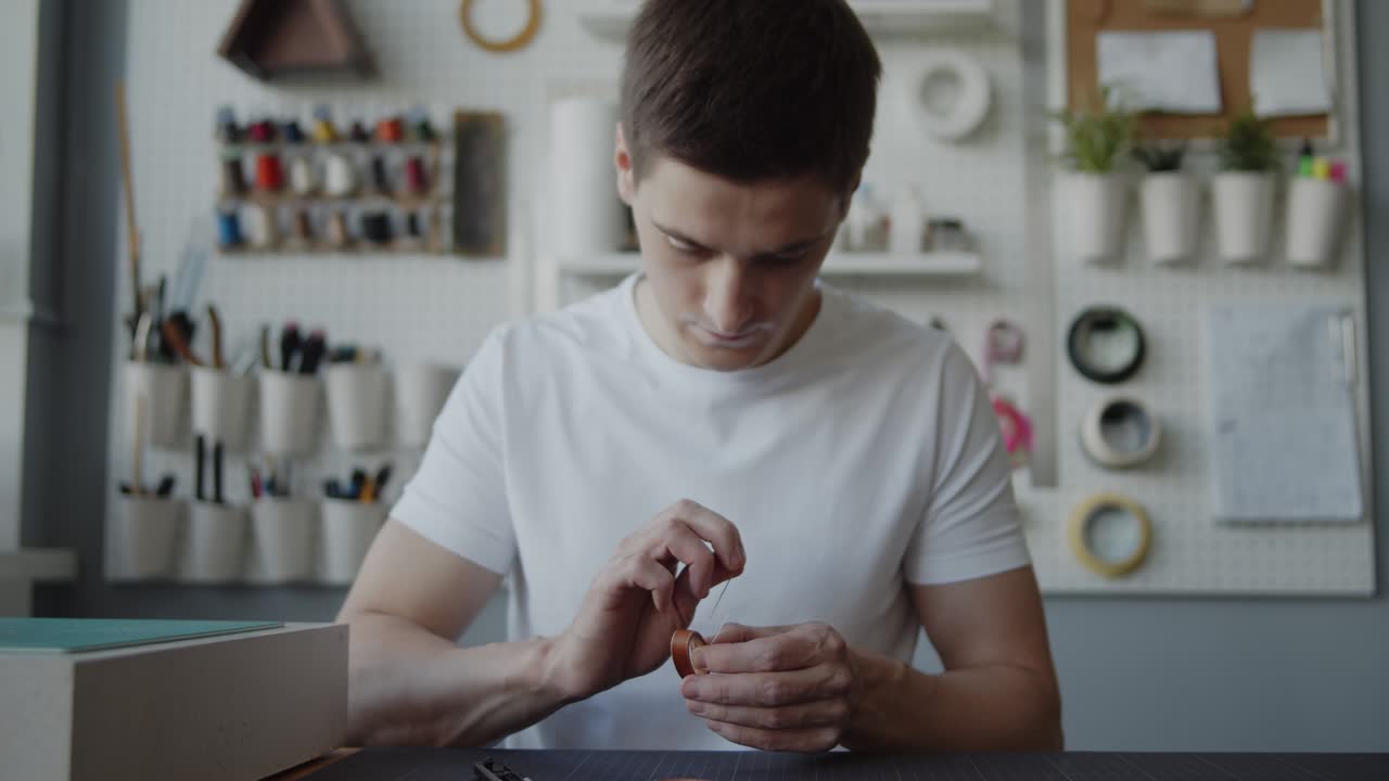 joven trabajador del cuero con vitiligo cosiendo a mano un bucle de cuero para un cinturón